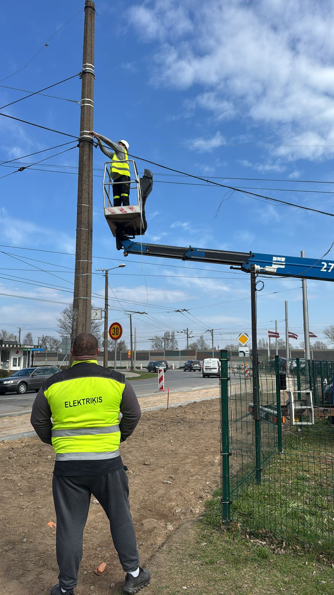 Elektriķis ar ELEKTRIĶIS vesti uzrauga kolēģa darbu pacēlājā