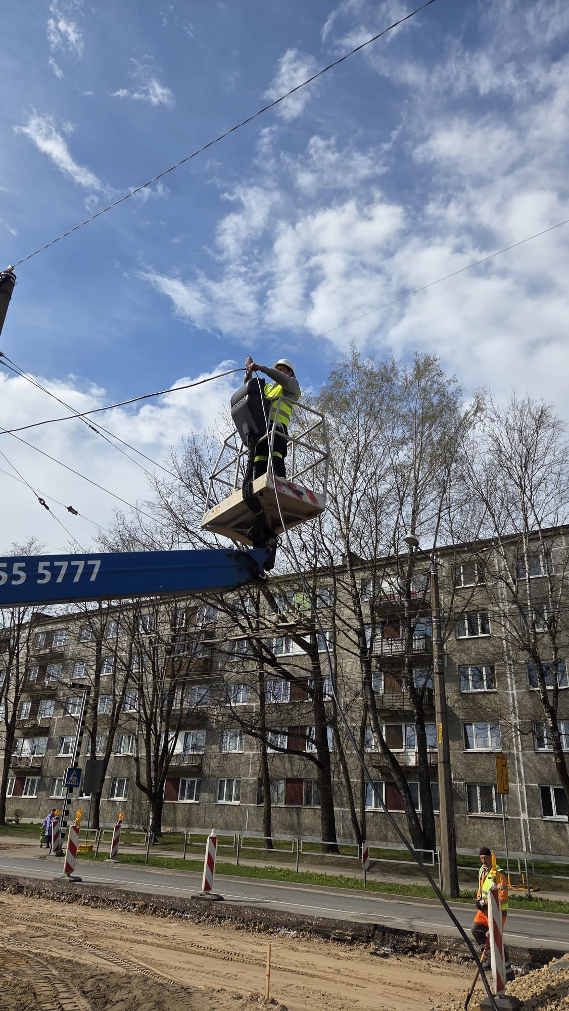 Elektriķis strādā pacēlājā, pieslēdz kabeļus pie koka staba