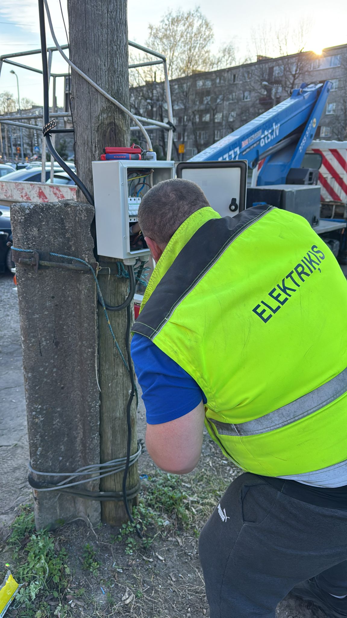 Elektriķis montē āra sadales kasti uz koka staba, vakara gaisma